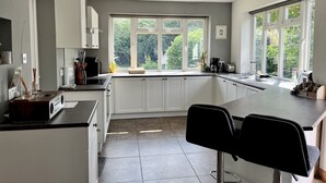 Una cocina moderna con armarios blancos, un ventanal grande y una barra con dos taburetes.