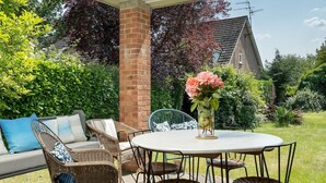 Un patio al aire libre con mobiliario de mimbre, una mesa redonda y un jarrón con flores.