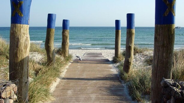 A wooden boardwalk leading to a beach with blue-painted posts marked with 'X'. - 18 Ferienwohnung im Fritz-bleyl-weg 16a EG (Burg auf Fehmarn)