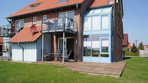 A two-story house with a red-tiled roof, a balcony, and a large window. - 18 Ferienwohnung im Fritz-bleyl-weg 16a EG (Burg auf Fehmarn)