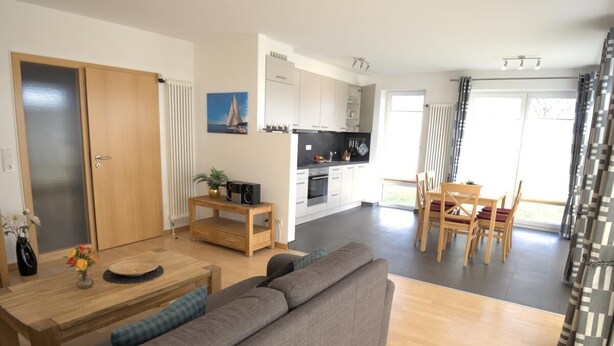 Un appartement moderne comprenant un salon, un coin repas et une cuisine. On y trouve un canapé, une table à manger avec des chaises, ainsi qu’une cuisine équipée de placards et d’appareils électrom énagers.