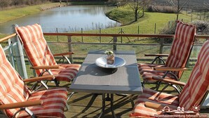 Une terrasse avec quatre chaises à rayures et une table, donnant sur une étendue d’eau et une zone herbeuse.