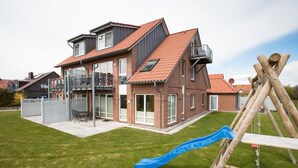 Une maison à deux étages avec un toit recouvert de tuiles rouges, un balcon et un toboggan dans le jardin.