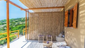 Un espace extérieur aménagé avec une zone de sièges couverte, comprenant deux chaises et une table, une clôture en bois et une vue sur la verdure.