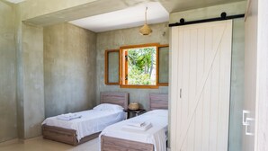 Une chambre avec deux lits simples, une grande armoire, une fenêtre donnant sur un espace verdoyant et un luminaire suspendu.