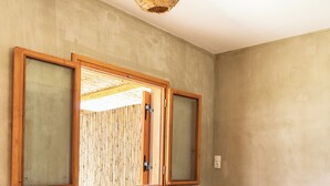 Une pièce moderne avec un canapé foncé, un luminaire suspendu en fibres tressées et une grande fenêtre dotée de stores en bambou.