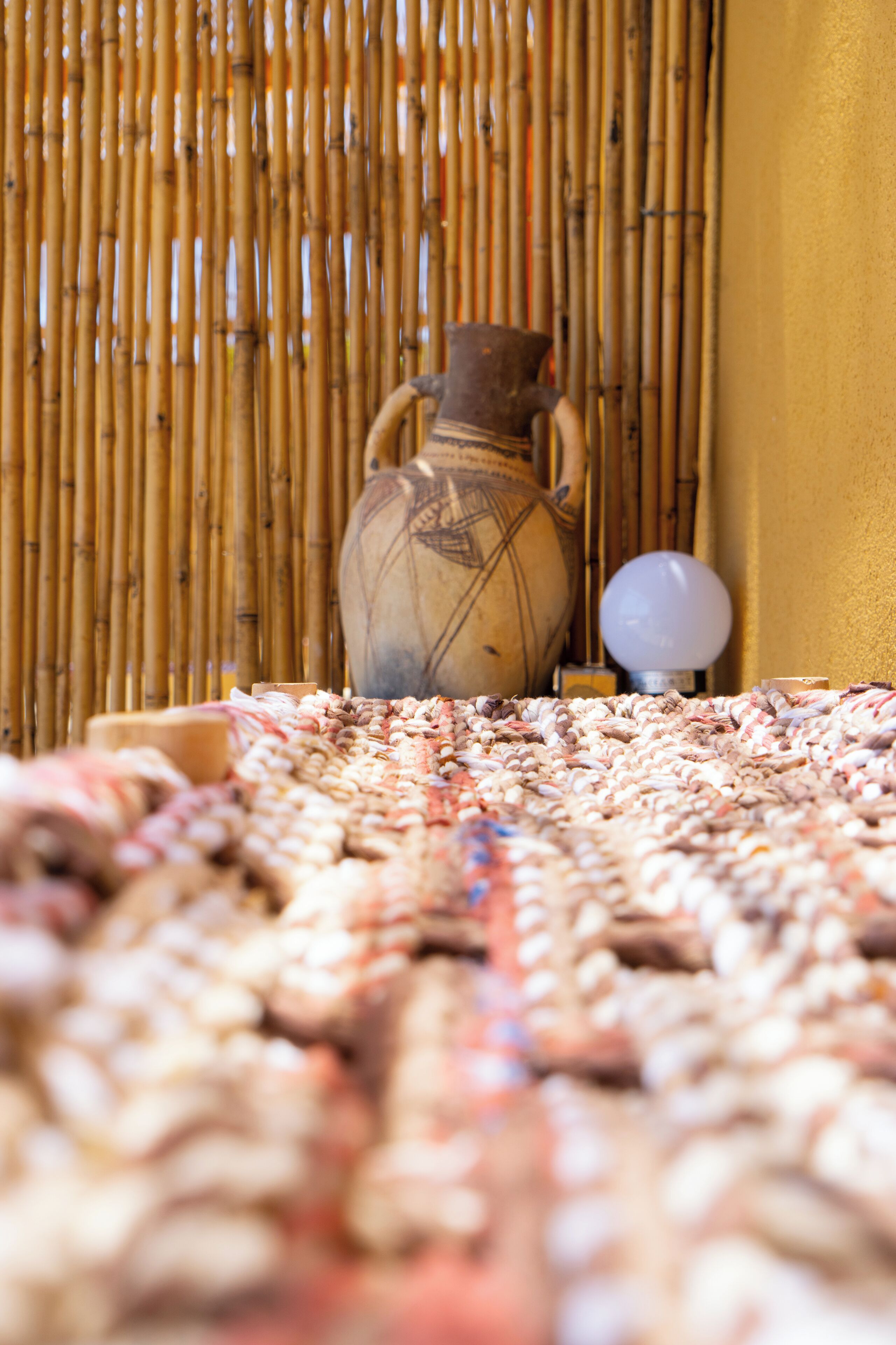 A bamboo wall, a ceramic vase, and a lamp on a patterned rug.