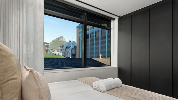 Ein Hotelzimmer mit Bett, Fenster mit Blick auf Gebäude und einen Berg, sowie einer dunklen Wand.