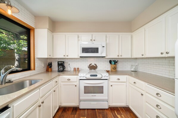 A kitchen with white cabinets, a stainless steel sink, a microwave, and an oven.