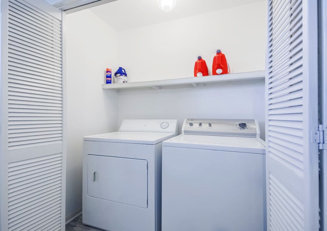 A laundry room with two washing machines and a shelf with detergent bottles.