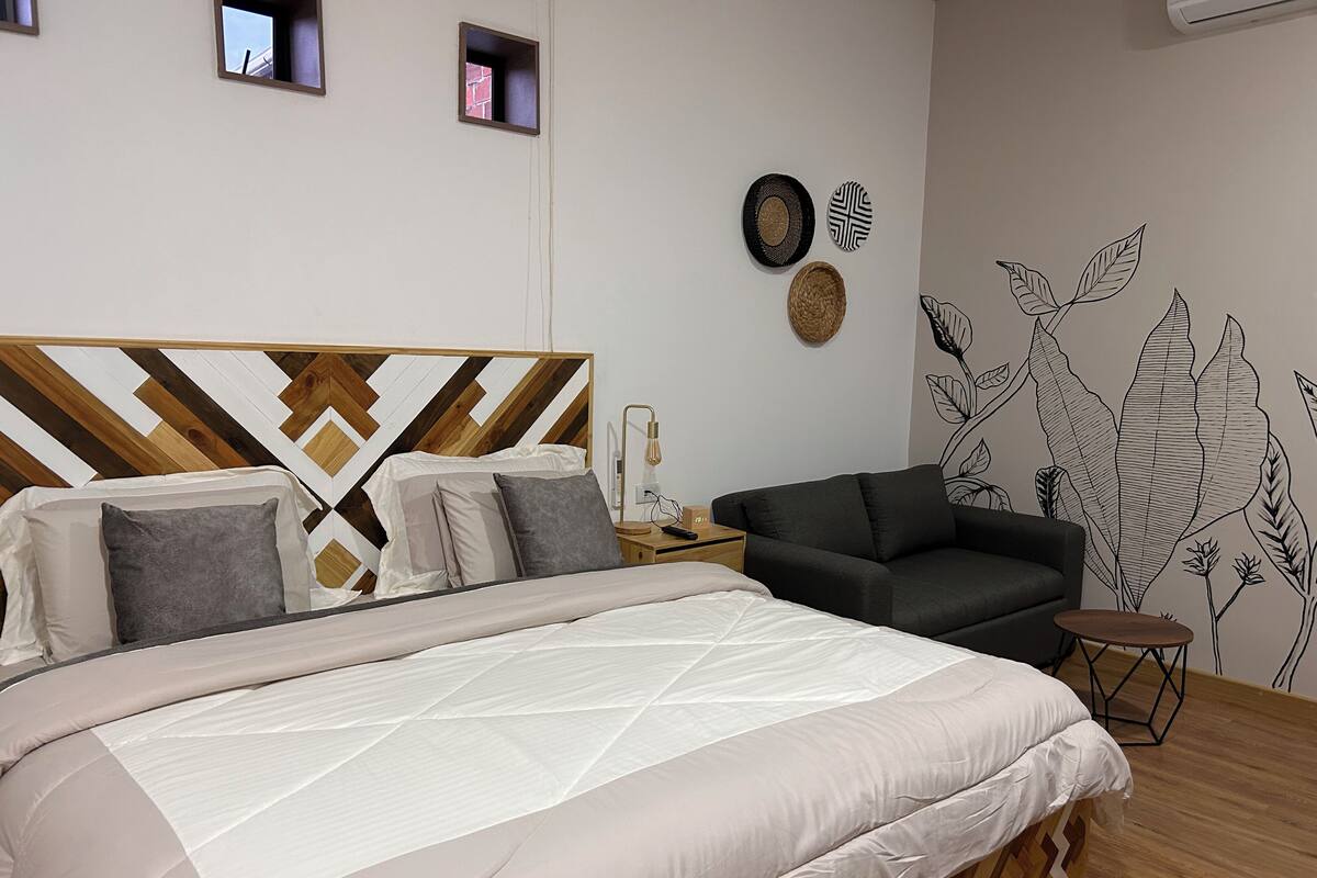 Un dormitorio moderno con una cama grande, un sofá oscuro y un mural en la pared.