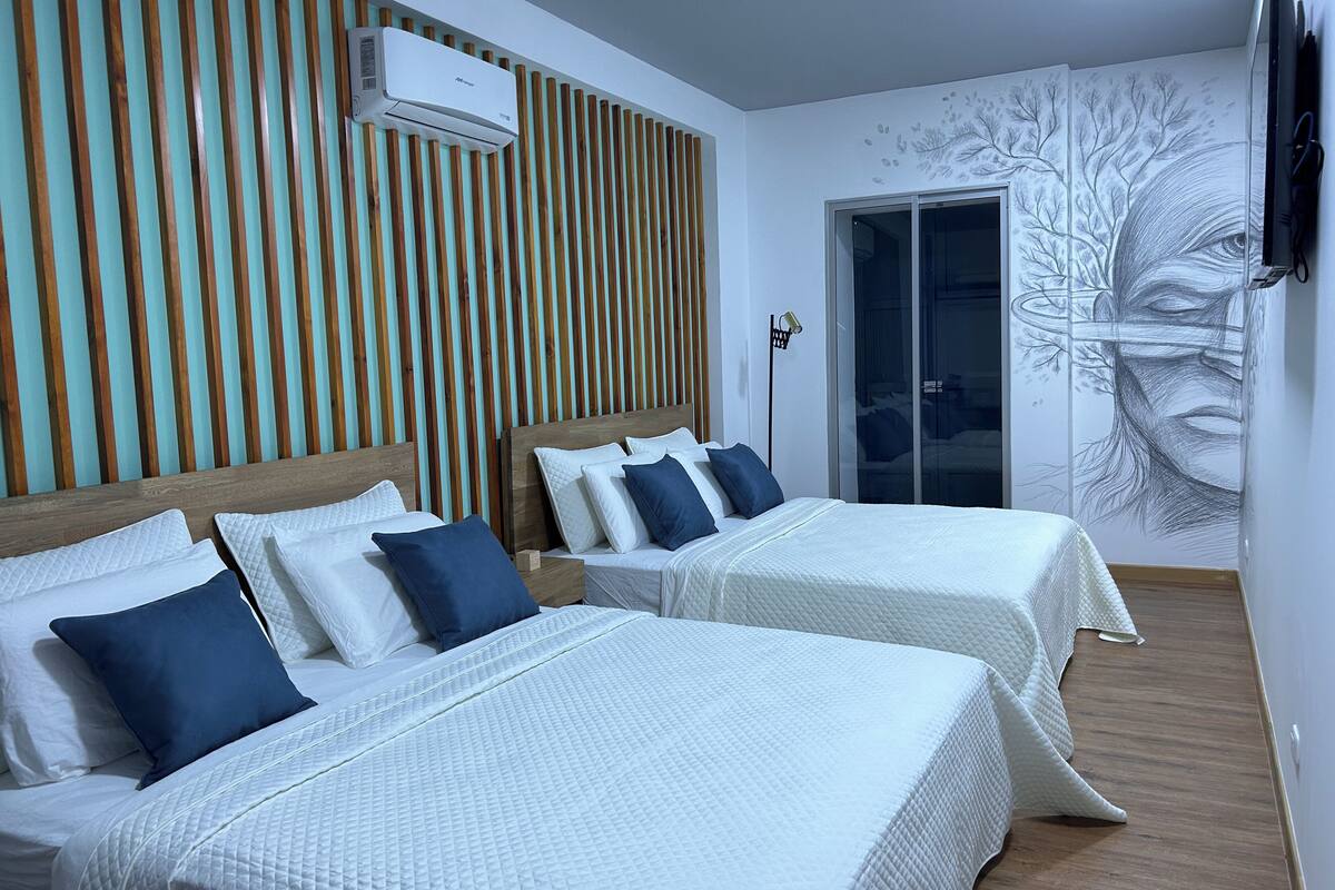 Habitación de hotel con dos camas, un panel de pared de listones de madera, un equipo de aire acondicionado y un mural.