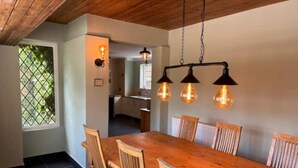 A dining area with a wooden table and chairs, a hanging light fixture, and a window with a view of greenery. - Charming Group Stay – Peaceful Retreat near London (Bexley,)