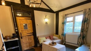A cozy room with wooden flooring, a white table with a lace tablecloth, a bench, a wooden door, and a window with curtains. - Charming Group Stay – Peaceful Retreat near London (Bexley,)