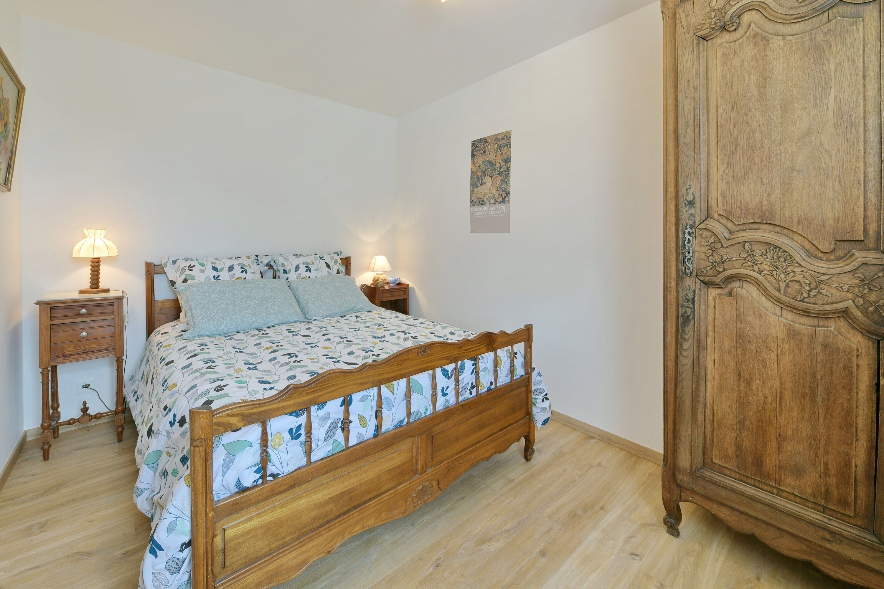 A bedroom with a wooden bed, two bedside tables with lamps, a wooden wardrobe, and a poster on the wall.