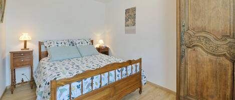 A bedroom with a wooden bed, two bedside tables with lamps, a wooden wardrobe, and a poster on the wall.