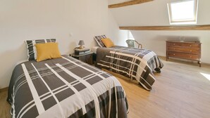 A bedroom with two beds, a wooden dresser, a chair, and a skylight.