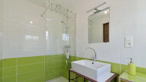 A bathroom with a glass shower enclosure, a white sink with a marble countertop, and a mirror above the sink.