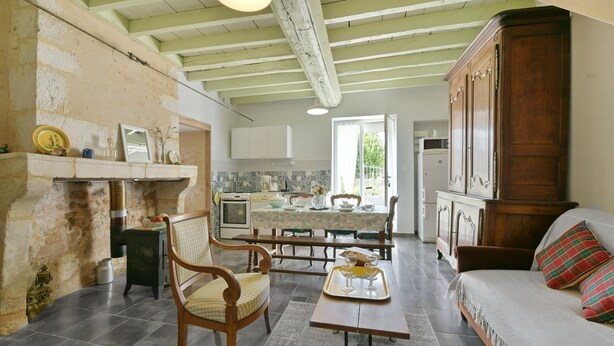 A spacious living room with a sofa, a dining table with chairs, a fireplace, and a kitchen in the background.