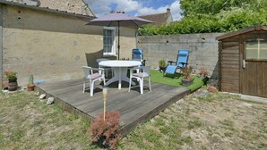 A patio with a round table and chairs, a wooden deck, and a small garden area with potted plants.