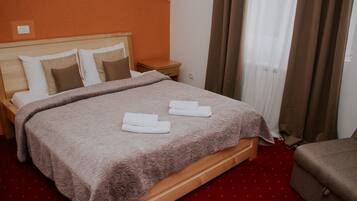 A neatly made bed with a patterned blanket and pillows, a wooden nightstand, and a red carpeted floor.