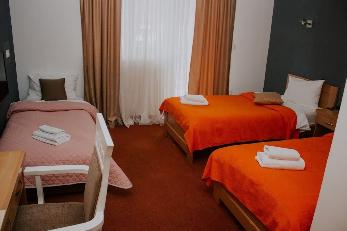 Quarto de hotel com duas camas, uma escrivaninha e uma cadeira.