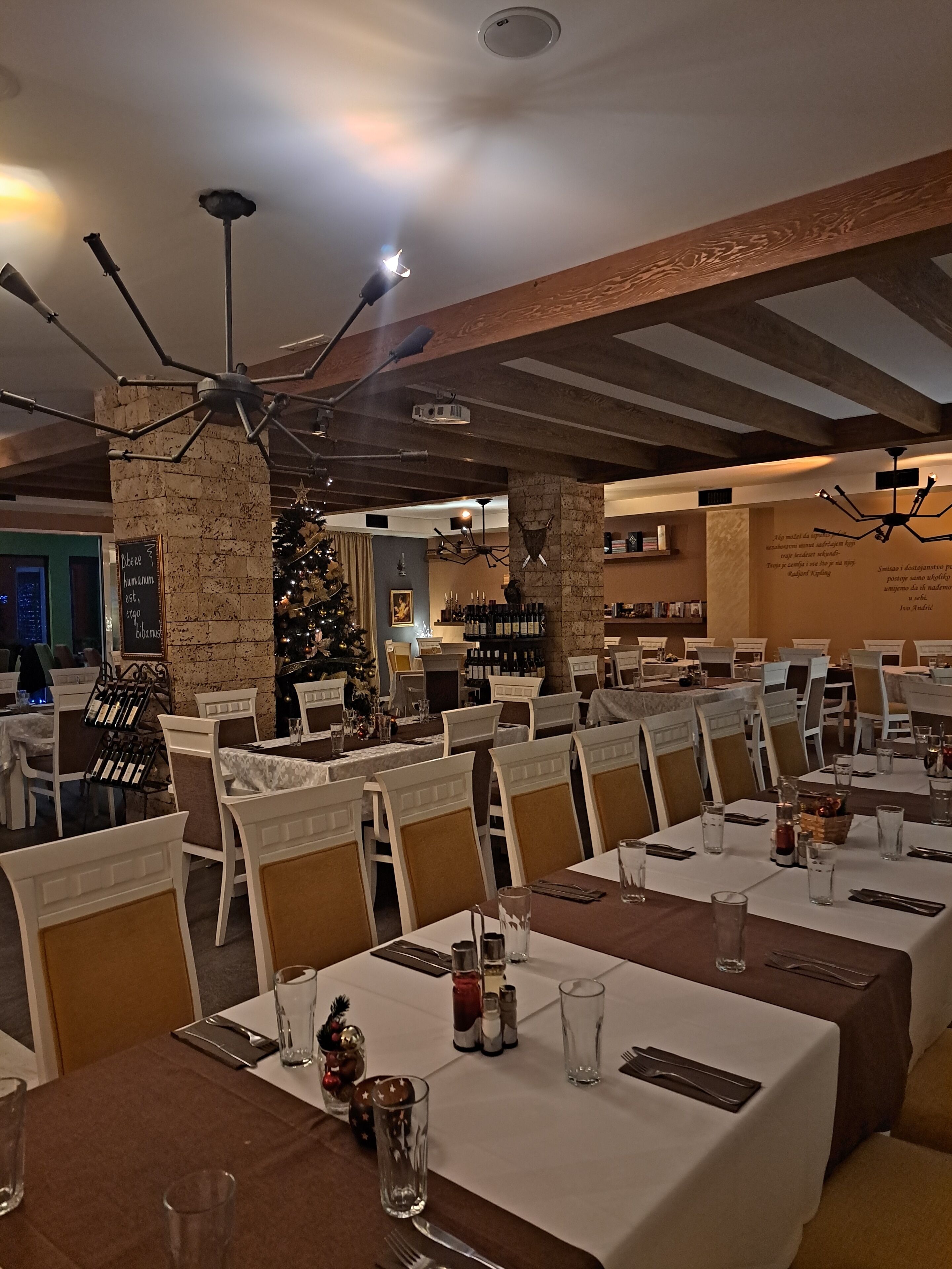 Un restaurante con varias mesas dispuestas para comer, un árbol de Navidad al fondo y un pilar de piedra con un letrero.