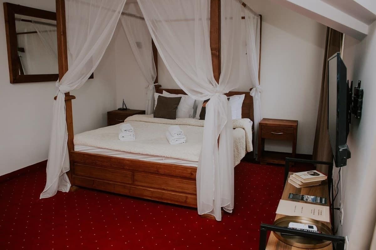 Quarto com uma cama de dossel, uma mesa de cabeceira de madeira e um tapete vermelho.