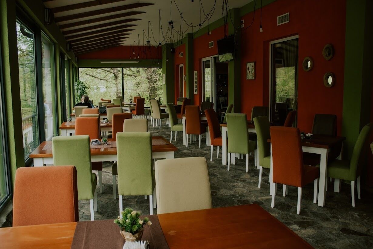 A restaurant with tables and chairs, large windows, and a stone floor.