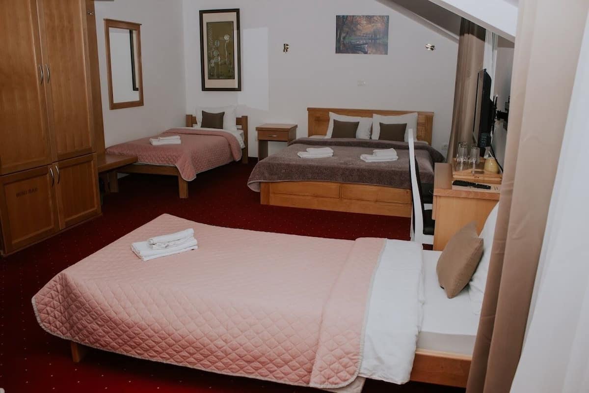 Quarto de hotel com duas camas, um guarda-roupa de madeira, um espelho e obras de arte nas paredes.