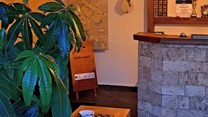 Un restaurante acogedor con una mesa de madera, sillas y una planta grande en maceta. Se ve una barra con una pared de piedra y luces colgantes al fondo.