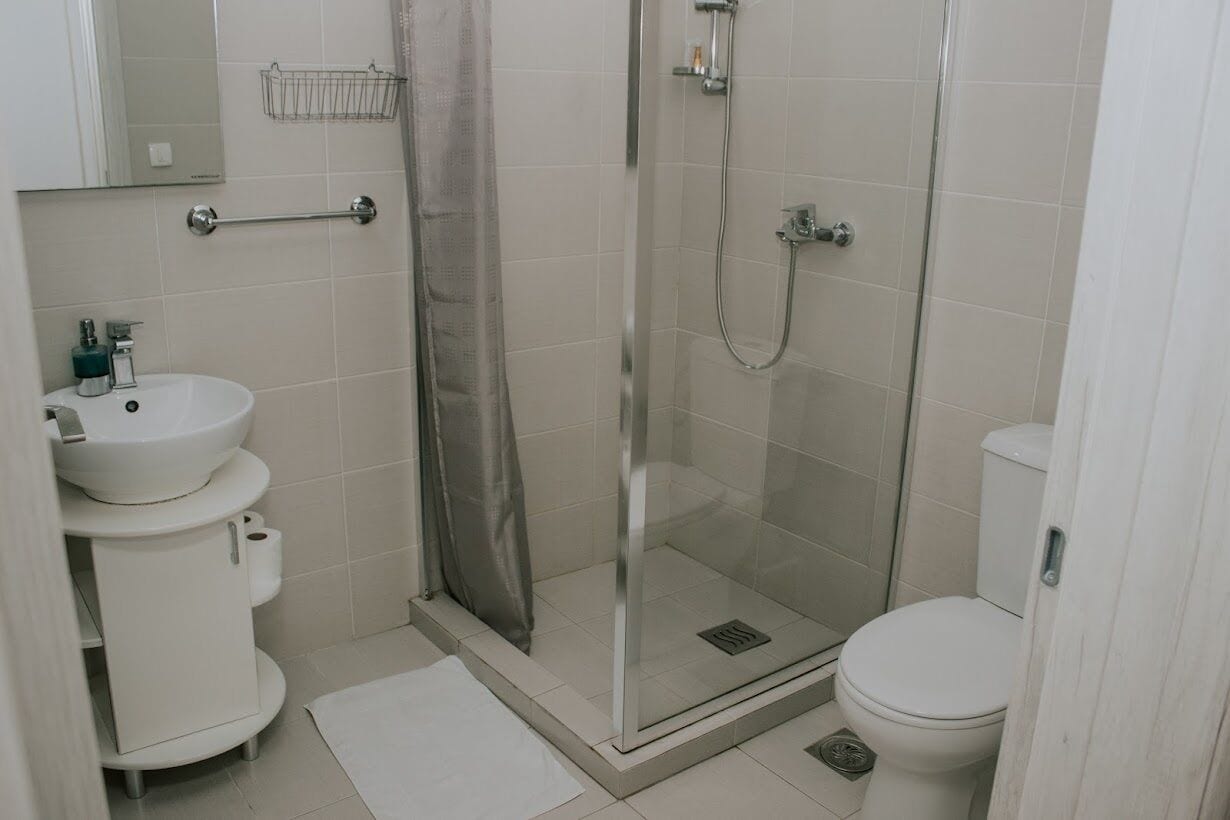 Un baño con ducha separada por mampara de vidrio, un lavamanos blanco y un inodoro.