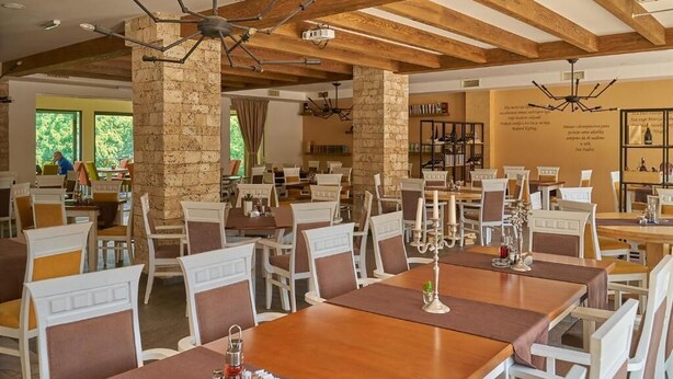 Un restaurante con vigas de madera y pilares de piedra, mesas con velas y vistas al exterior.