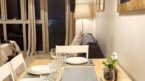 A dining area with a wooden table set for four, equipped with plates, glasses, and cutlery. There are two pendant lights above the table, and a large mirror on the wall.