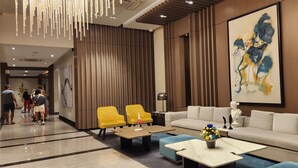 A modern hotel lobby with a beige sofa, yellow armchairs, a coffee table, and a large abstract painting.