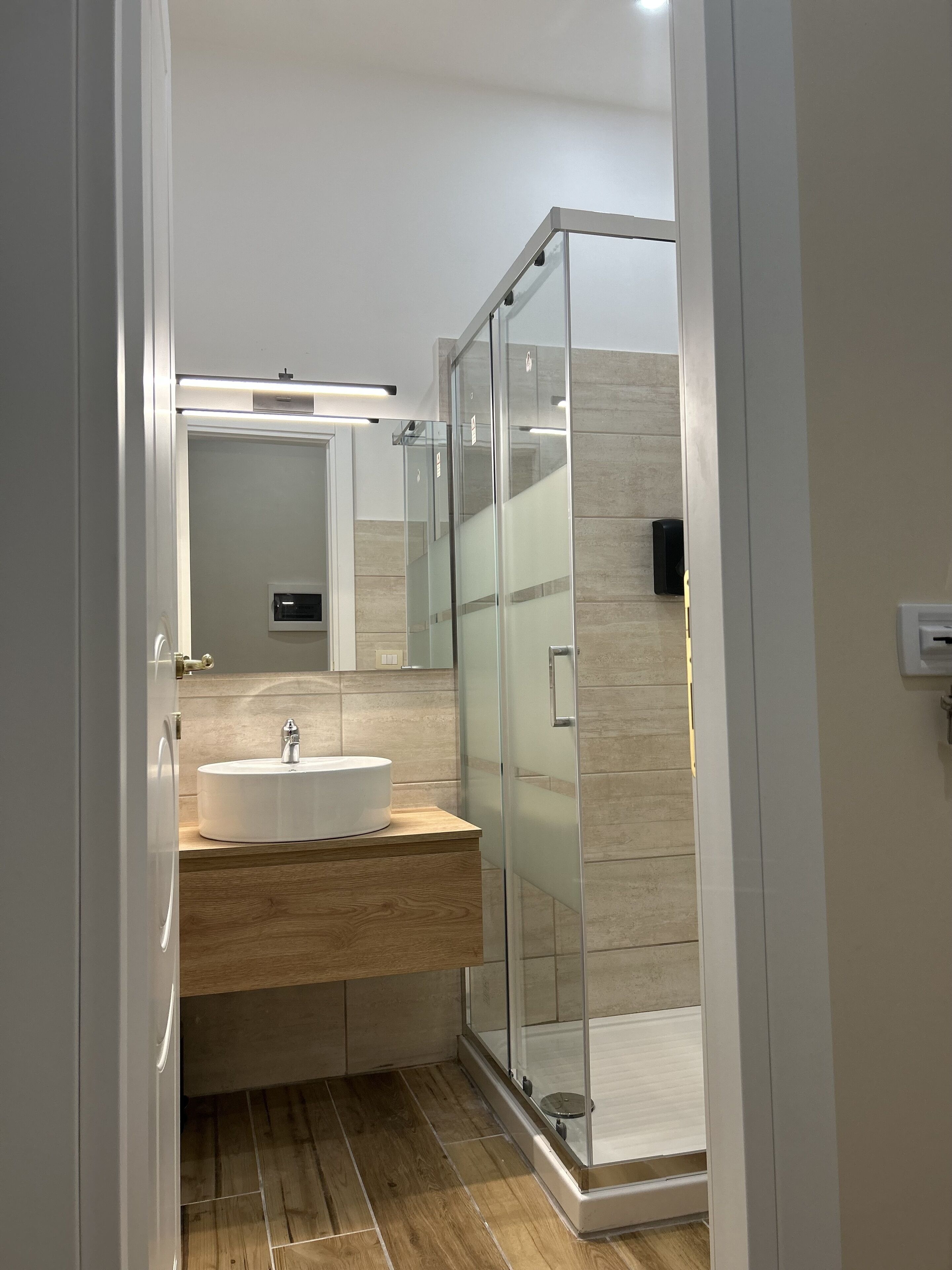 A modern bathroom with a glass shower enclosure, a wooden vanity, and a white sink.