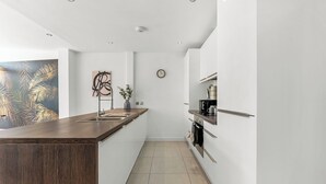 A modern kitchen with a wooden countertop, white cabinets, a clock, and a plant. - Modern Luxe Living in Lincoln - Flat 3 (Lincolnshire)