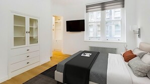 Makuuhuone, jossa on sänky, televisio, ikkuna, patteri ja vaatekaappi.