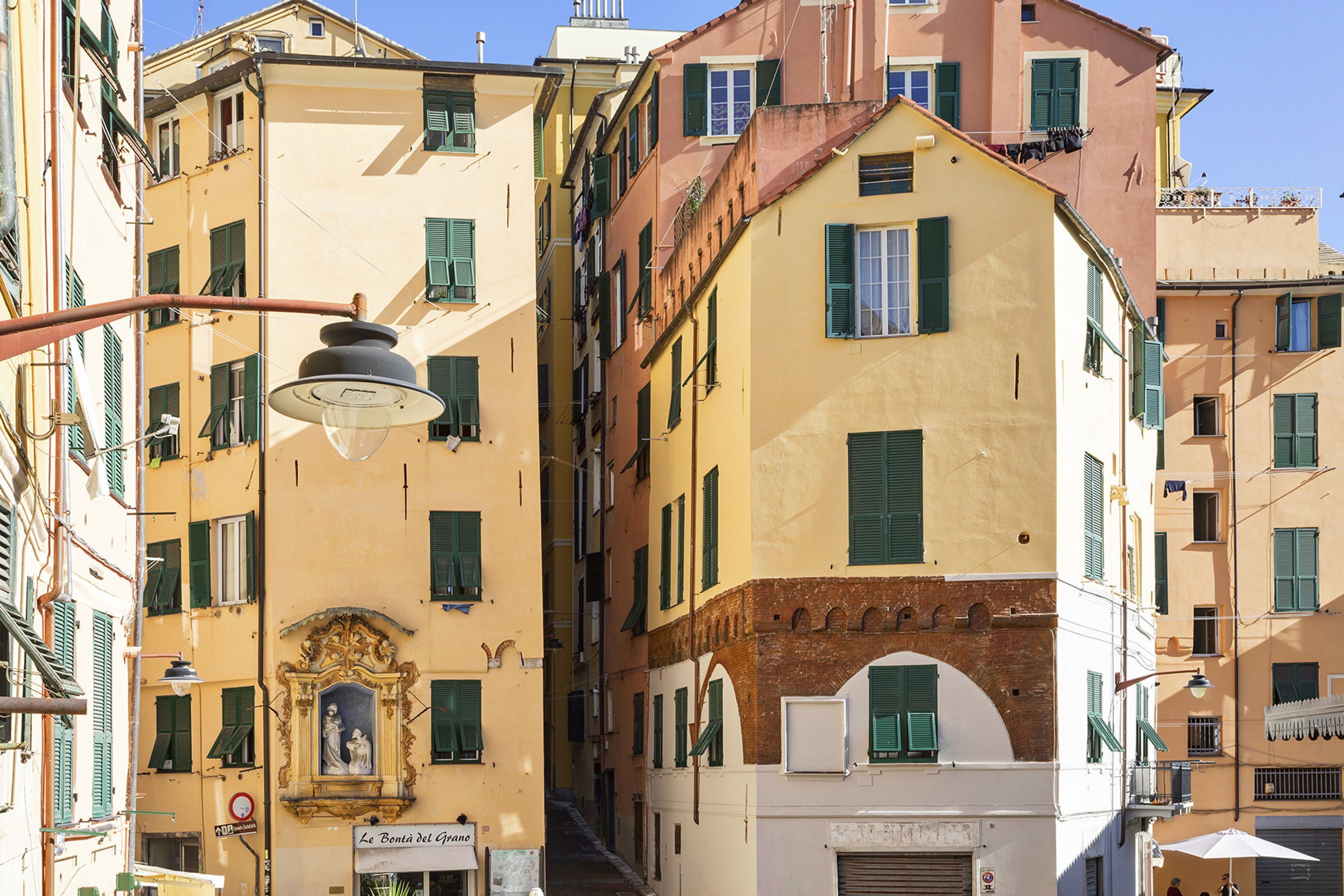 A narrow street with buildings featuring balconies and shutters.