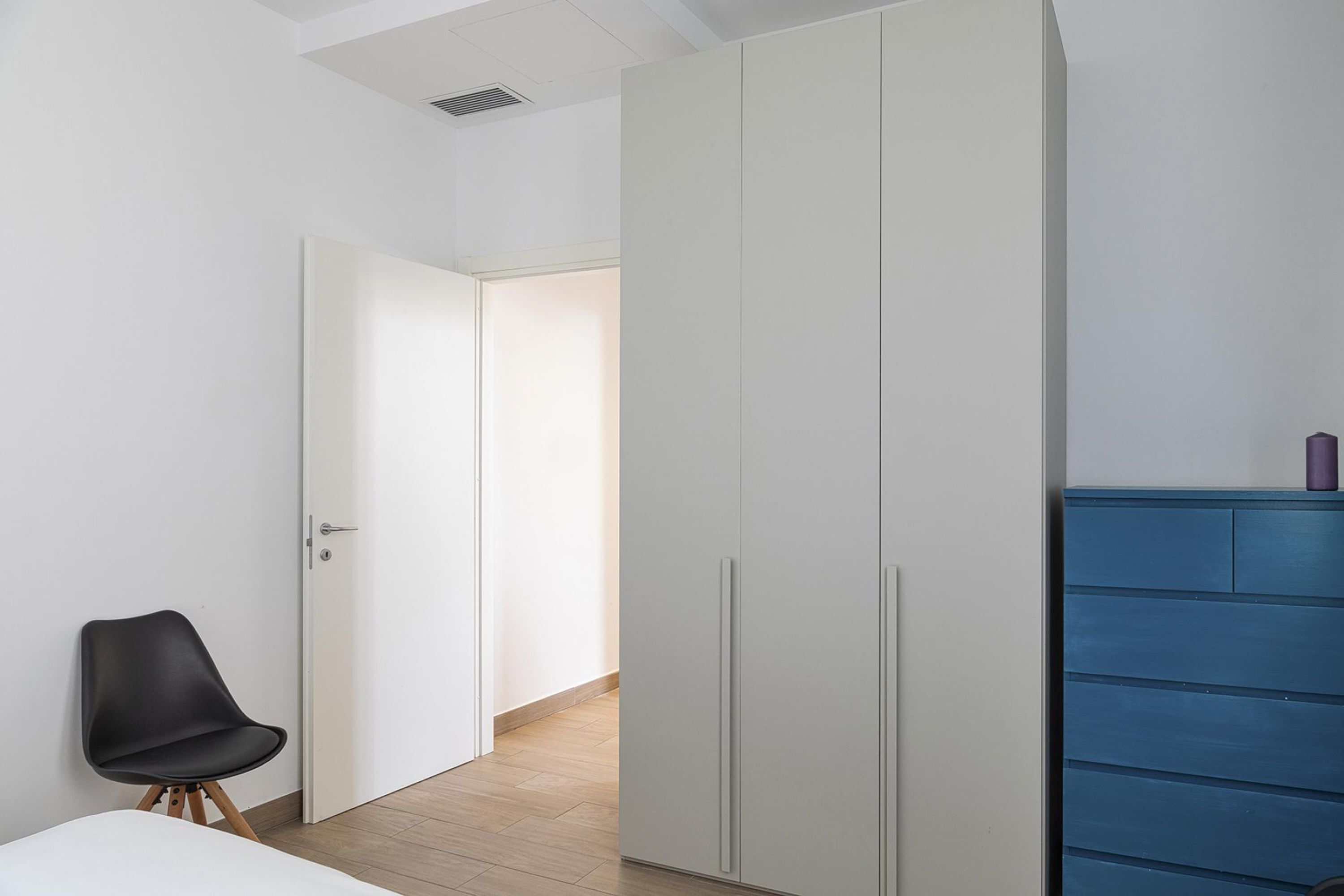 A bedroom with a bed, a black chair, a wardrobe, and a blue dresser.
