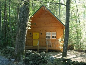 Une petite cabane en bois dotée d’un porche, entourée d’arbres et de rochers.