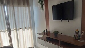 A modern living room with a flat-screen TV mounted on a wooden shelf, a sofa, and a ceiling fan. - Cozy apartment close to Canção Nova in Condomínio da Fé (Cachoeira Paulista)
