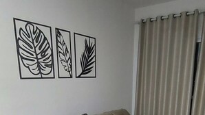 A beige sectional sofa with a cushion, a ceiling fan, and three framed leaf designs on the wall. - Cozy apartment close to Canção Nova in Condomínio da Fé (Cachoeira Paulista)