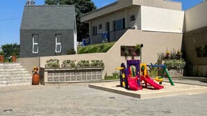 A modern building with a flat roof, a set of stairs leading to a gated entrance, and a playground with colorful slides. - Cozy apartment close to Canção Nova in Condomínio da Fé (Cachoeira Paulista)