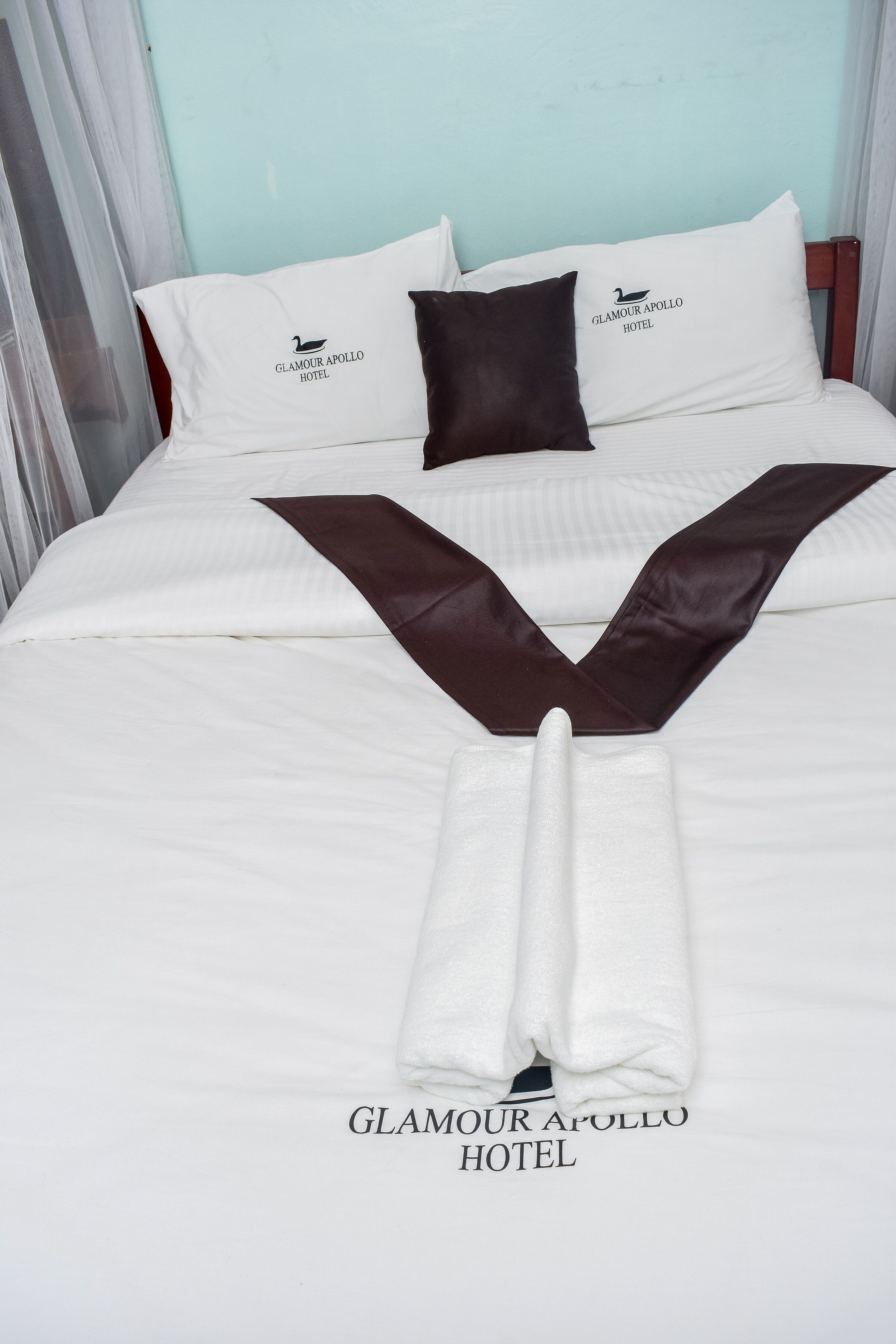 A neatly made bed with white and brown linens, pillows with the hotel logo, and a folded towel.