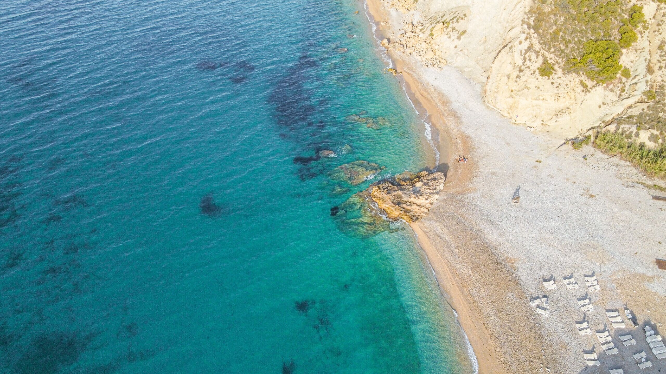 Une zone côtière caractérisée par des eaux turquoise et limpides, une plage de sable et des affleurements rocheux.