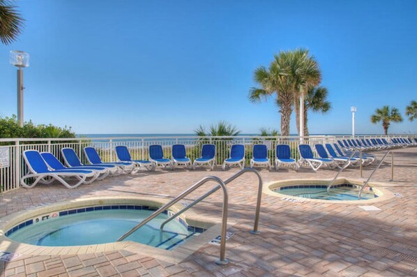 A poolside area with lounge chairs and two hot tubs.