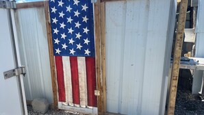 Una cerca de metal corrugado con estructura de madera y una bandera estadounidense pintada.