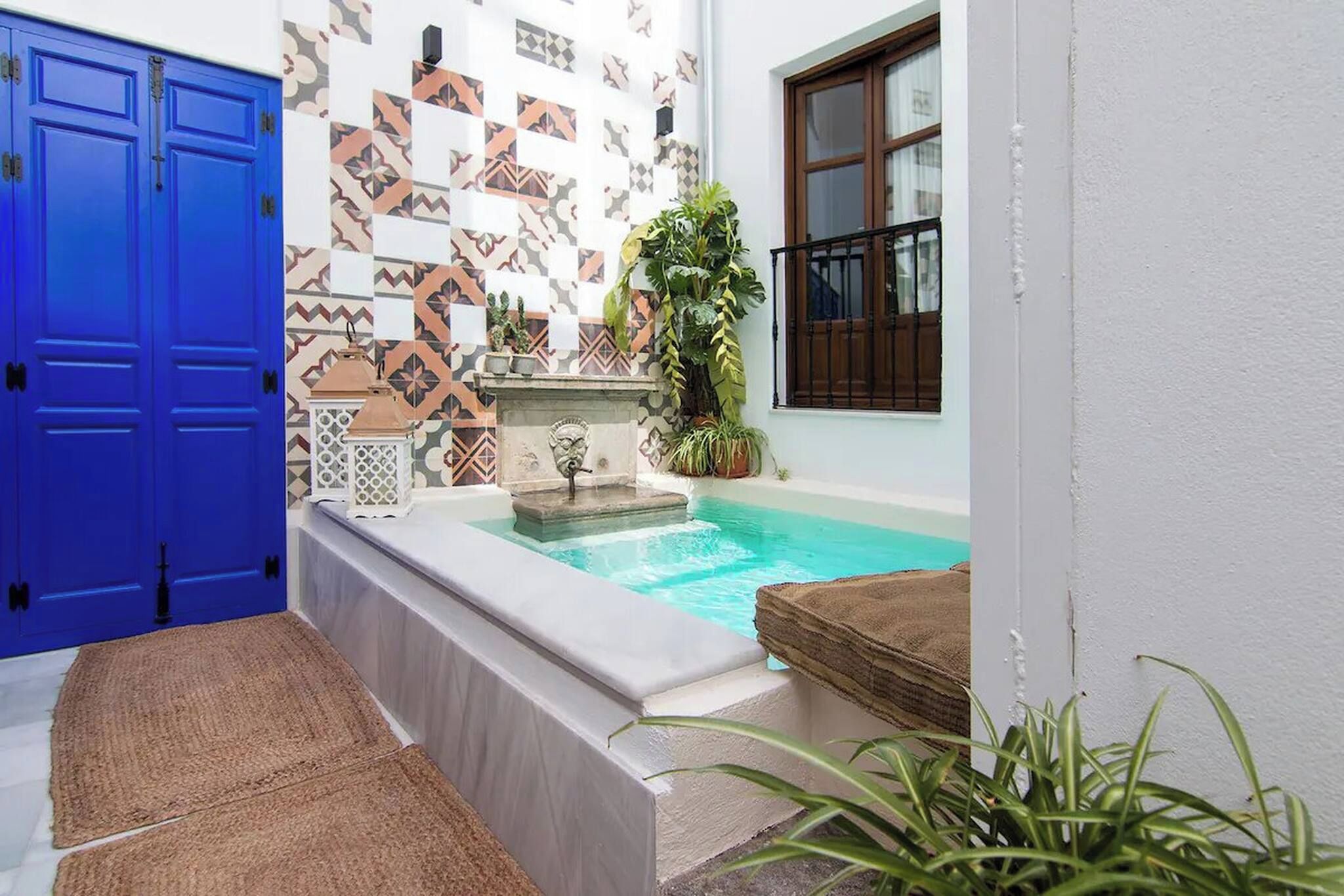 Zona de piscina con un muro de azulejos, una puerta azul y una ventana con vistas.