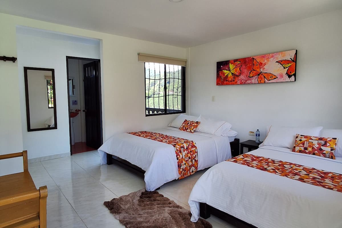 A hotel room with two beds, a wooden chair, a mirror, a window, and a painting.